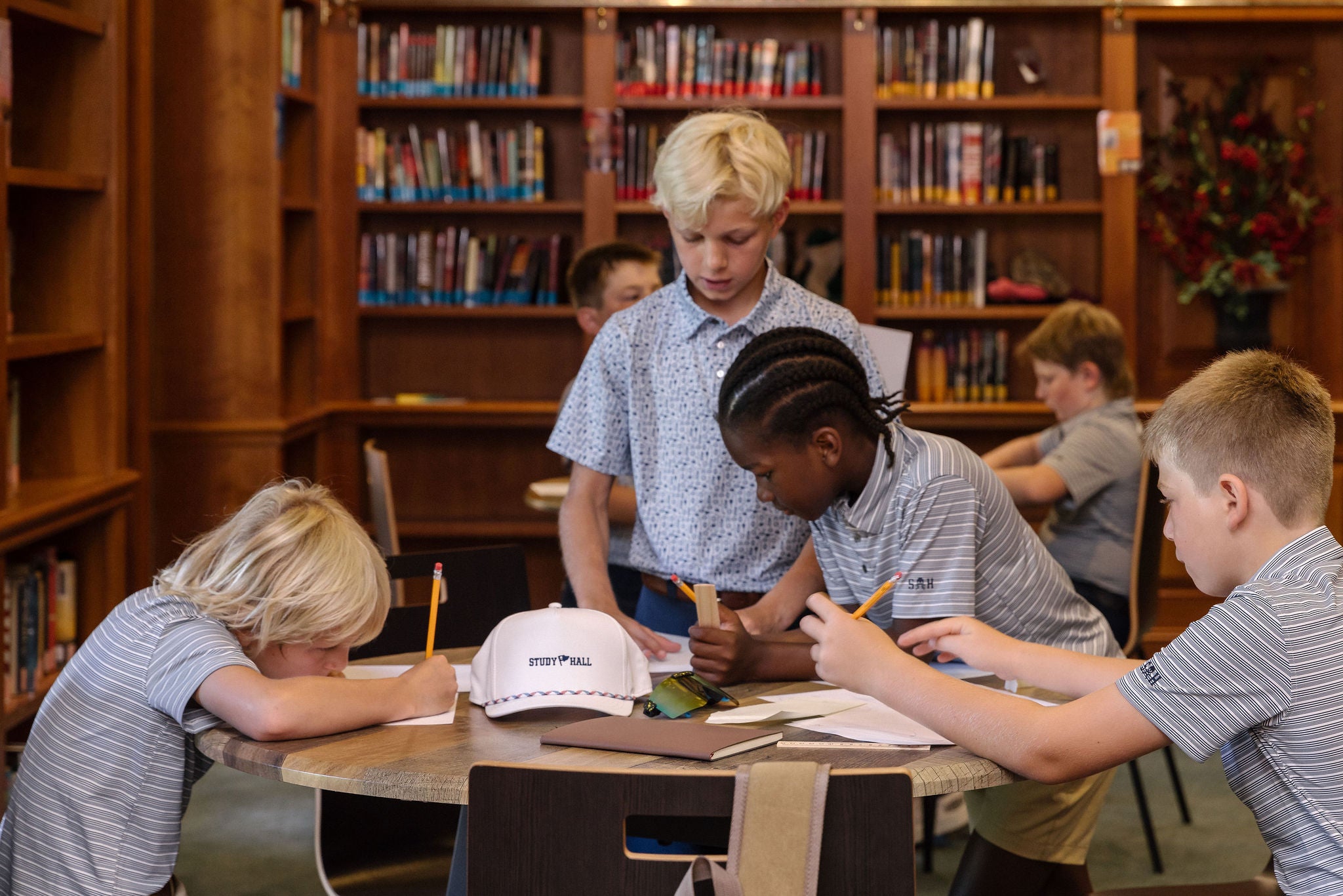 Children sitting at a table in a library setting with books on shelves in the background.