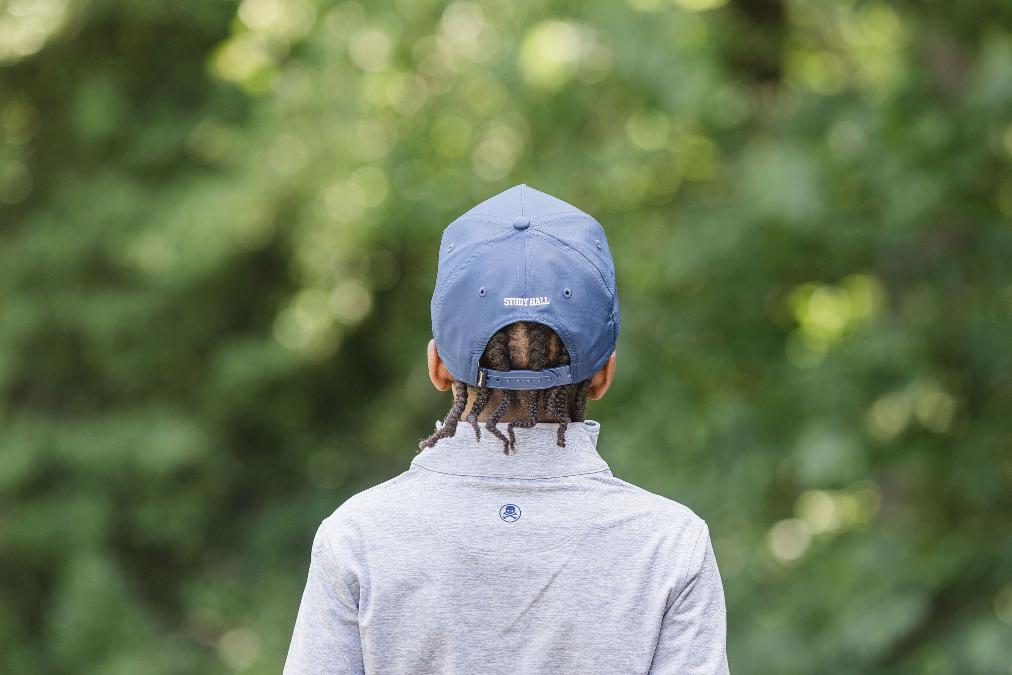 Young boy wearing navy ball cap and gray quarter zip in front of gray blurred background