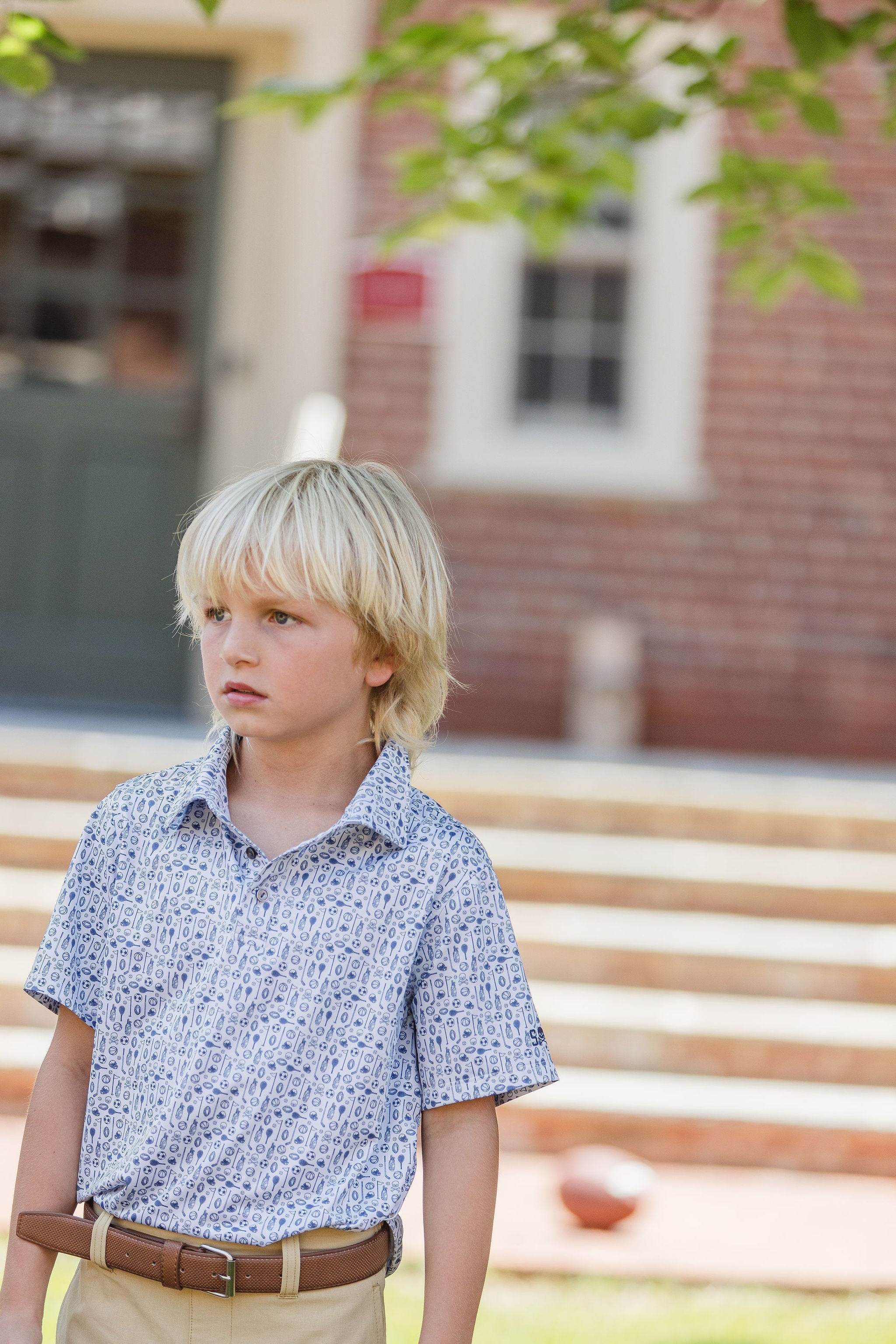 Young blonde haired boy wearing patterned polo top in front of school steps