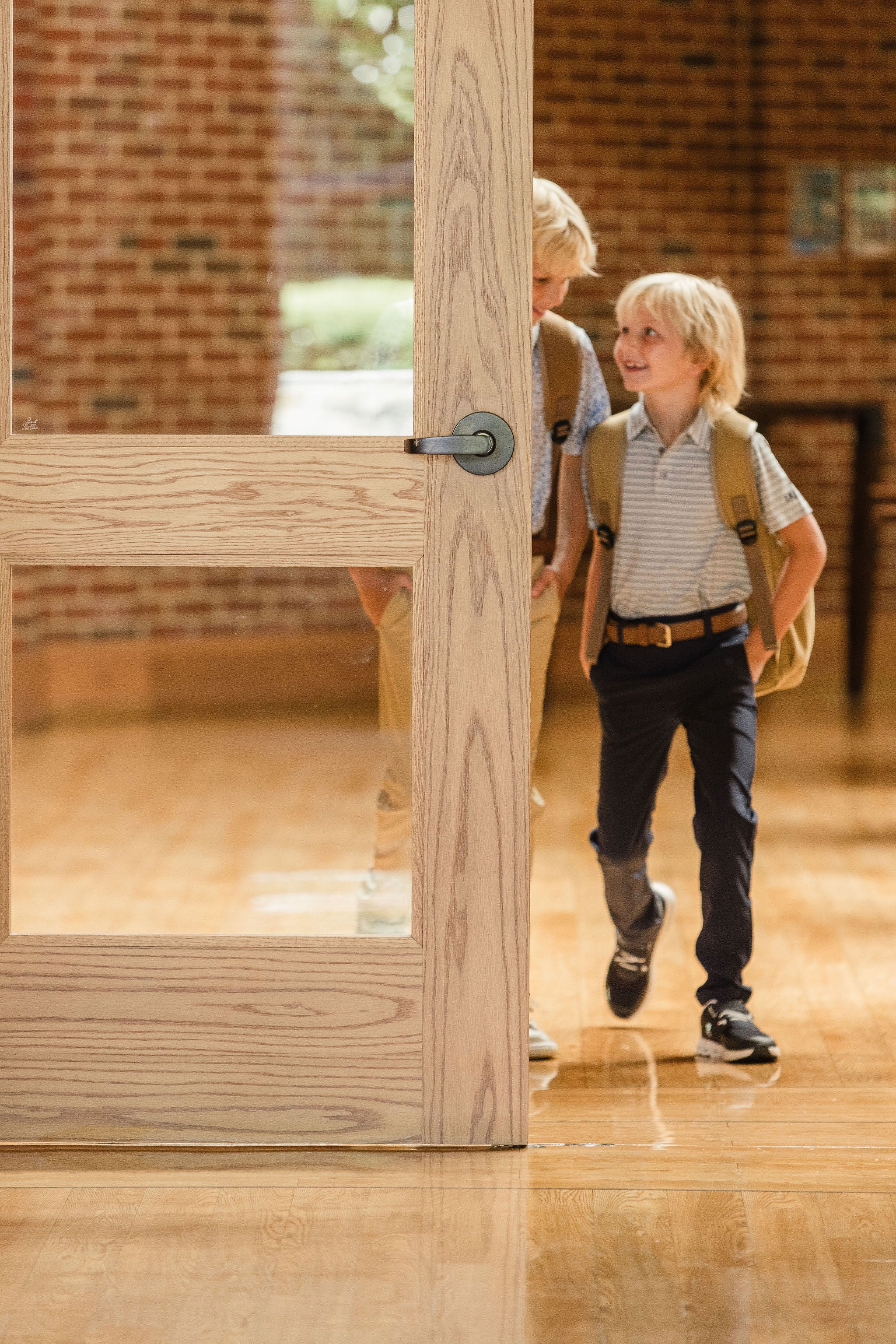 Young boys wearing backpacks, navy pants, and striped polos in private school