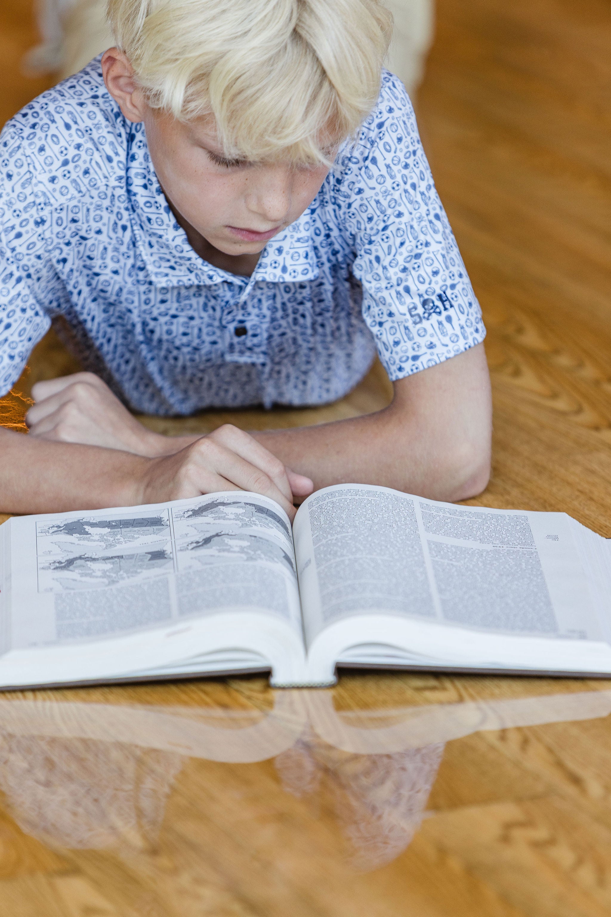Child reading an open book on a wooden floor