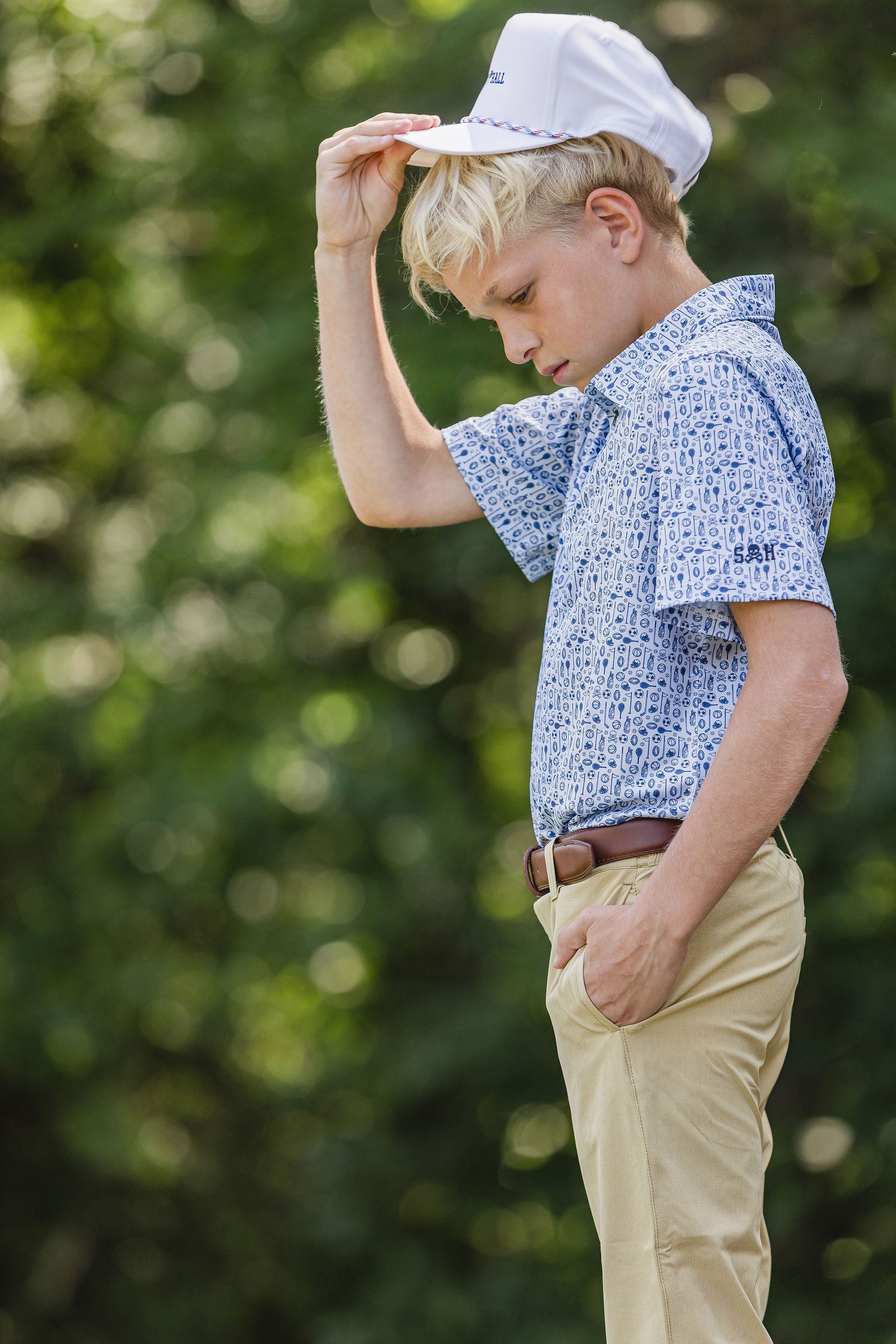 Young boy adjusting a cap outdoors with a blurred green background