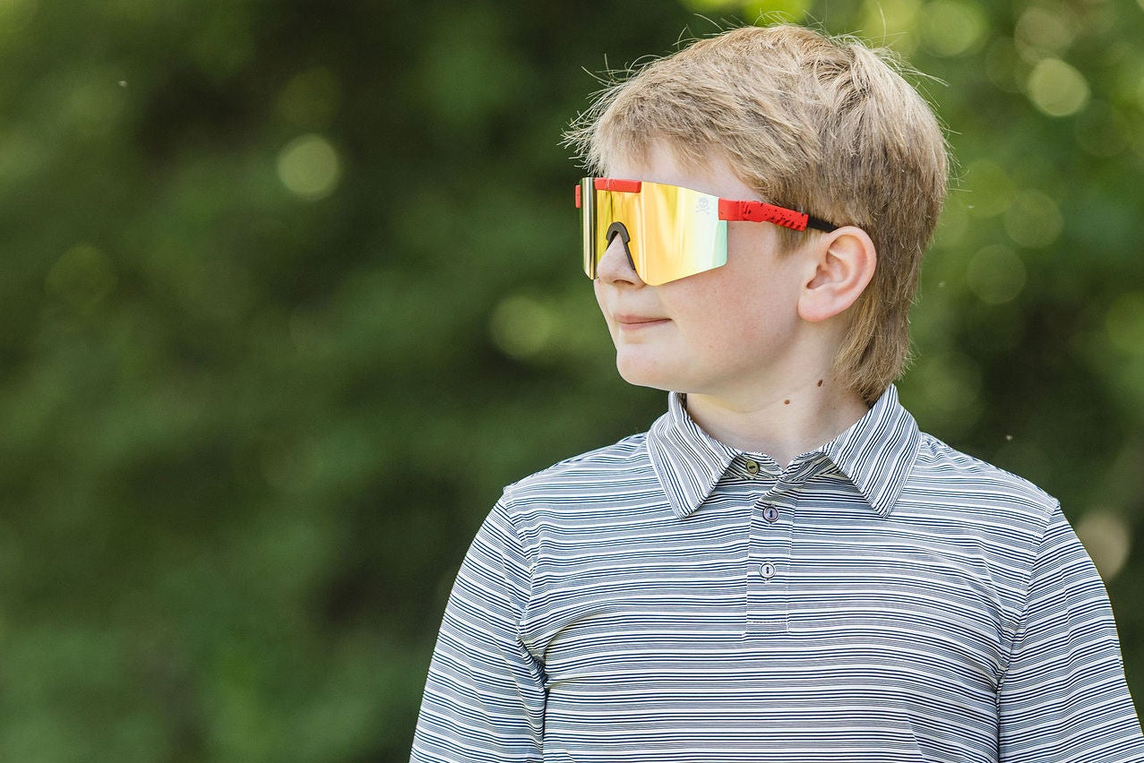 Young boy wearing a striped polo shirt and reflective sunglasses outdoors.