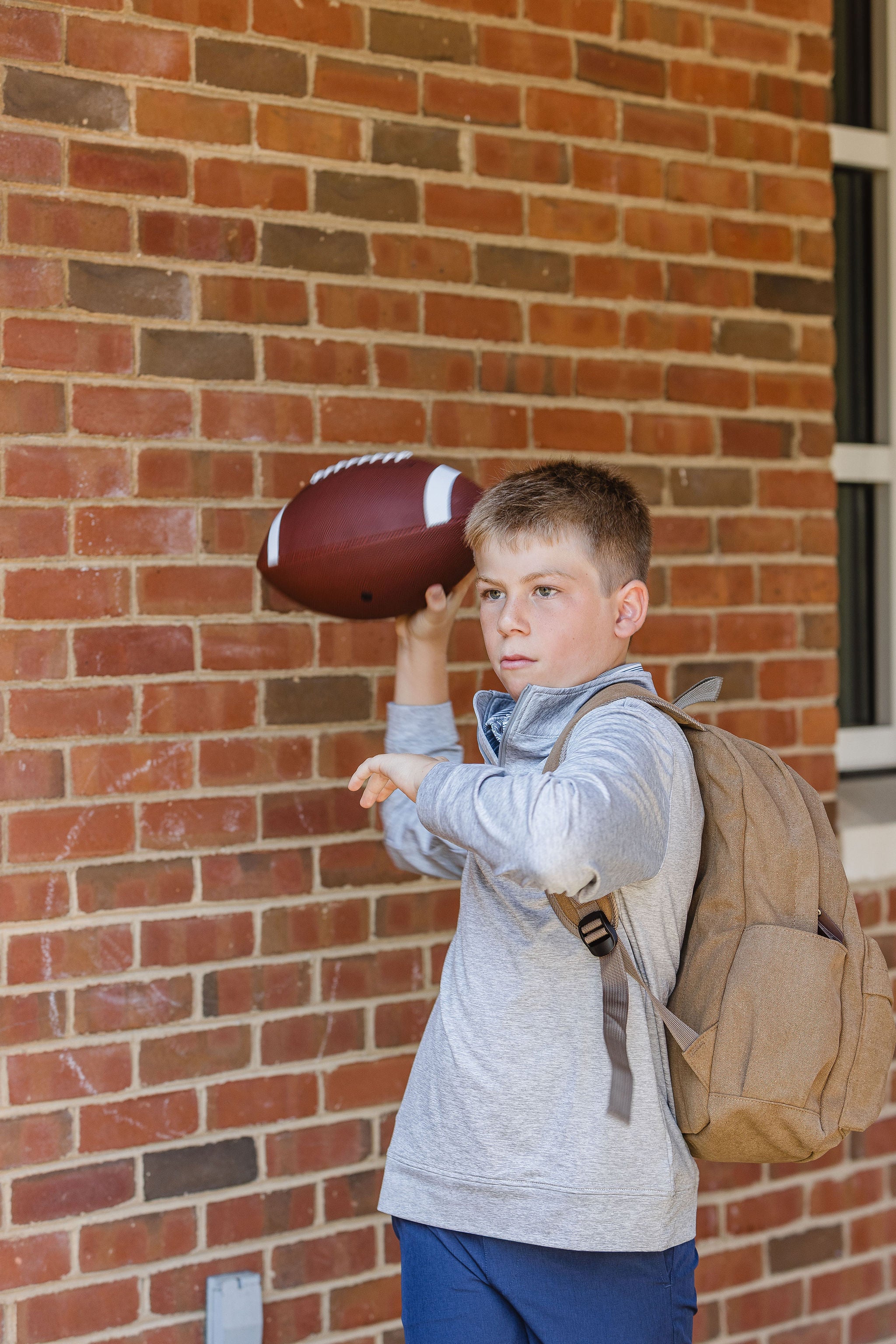 Young boy throwing a football against a brick wall