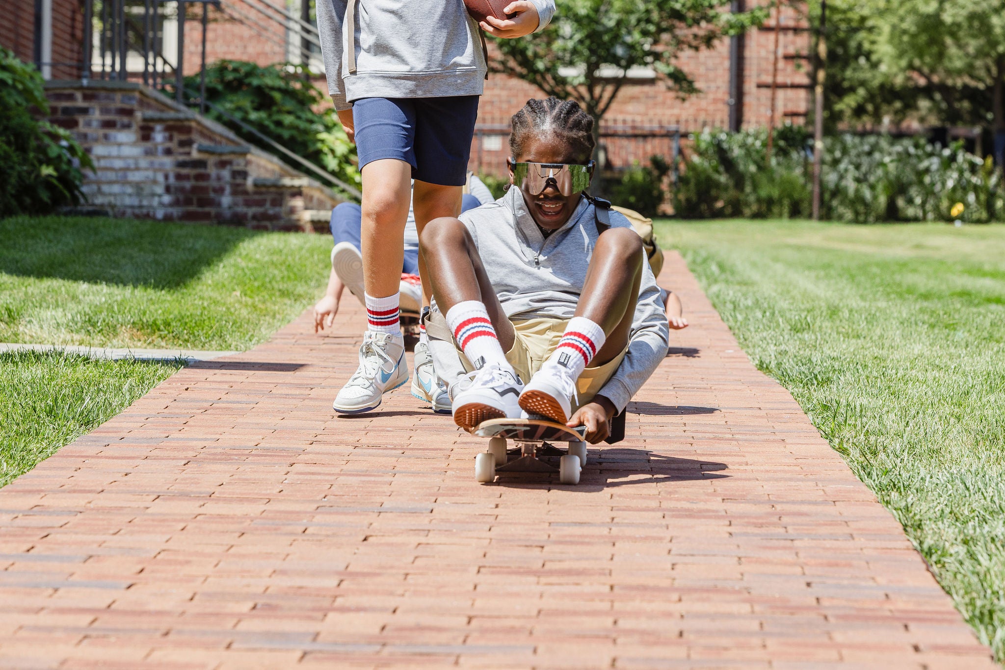 Two children riding skateboard on a brick path in a park