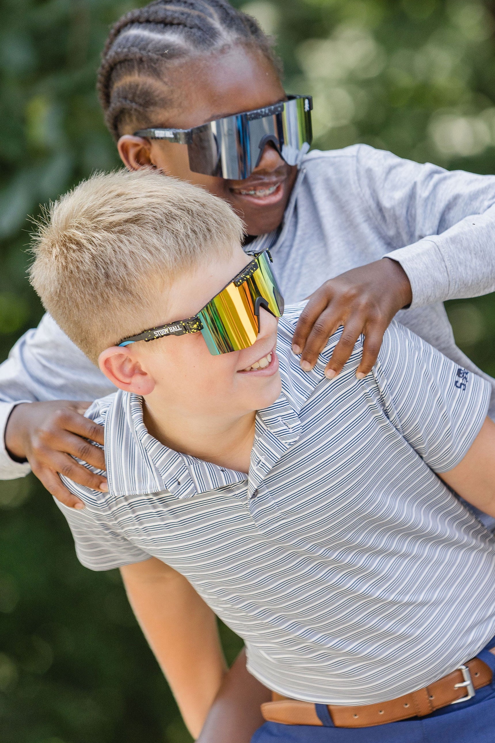 Two people wearing reflective sunglasses outdoors with greenery in the background