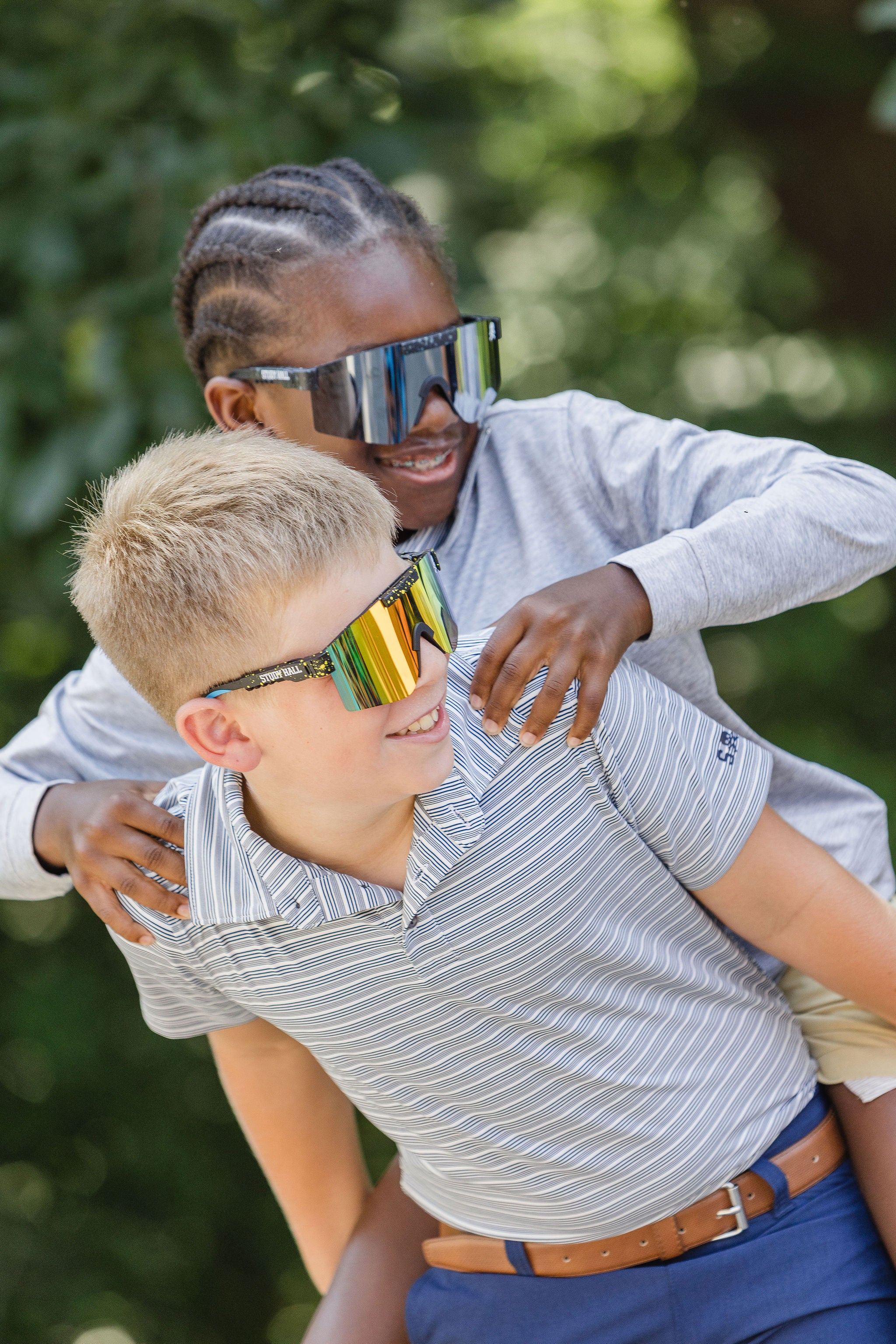 Two people wearing reflective sunglasses outdoors with greenery in the background