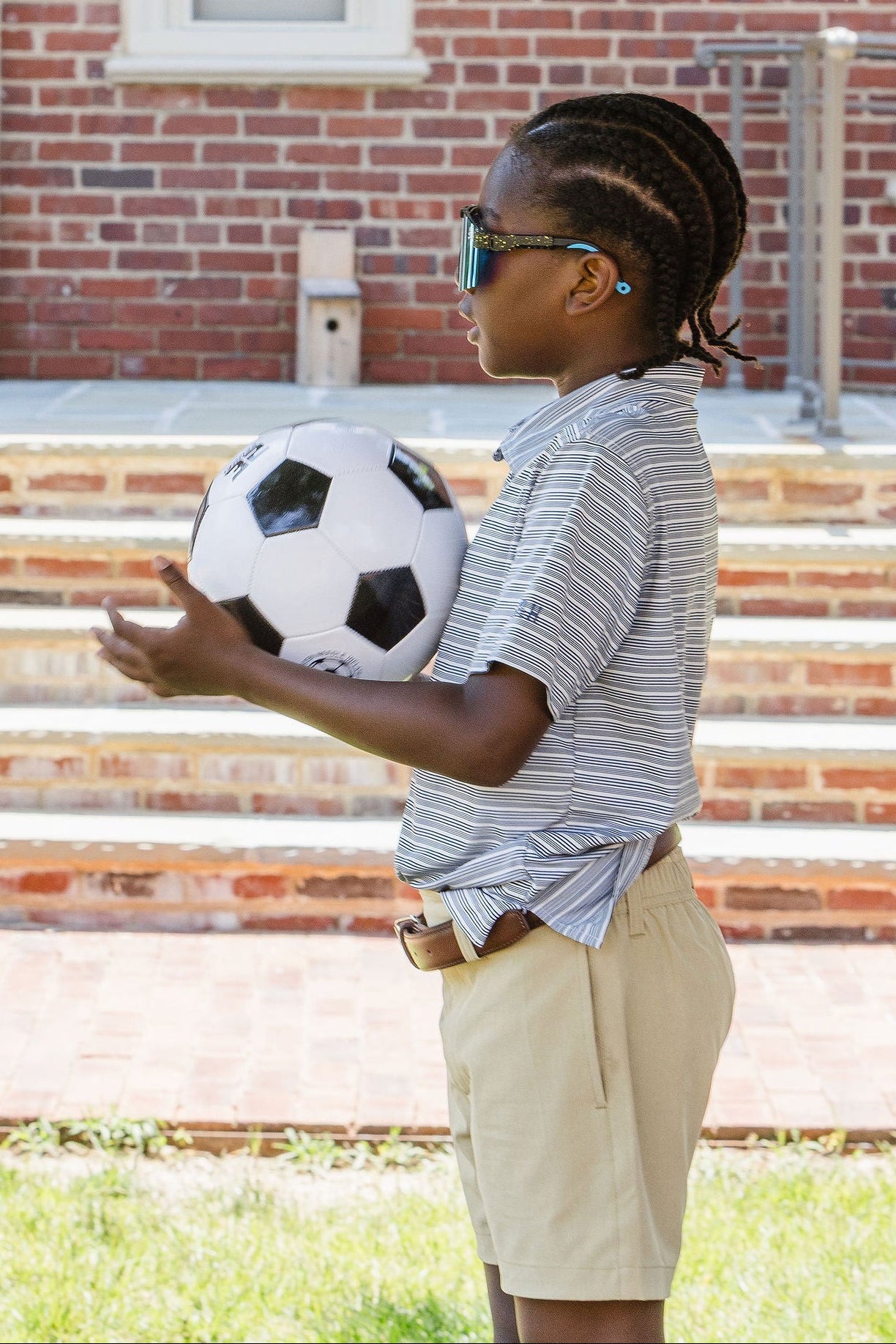 Young boy holding soccer ball in front of brick school steps
