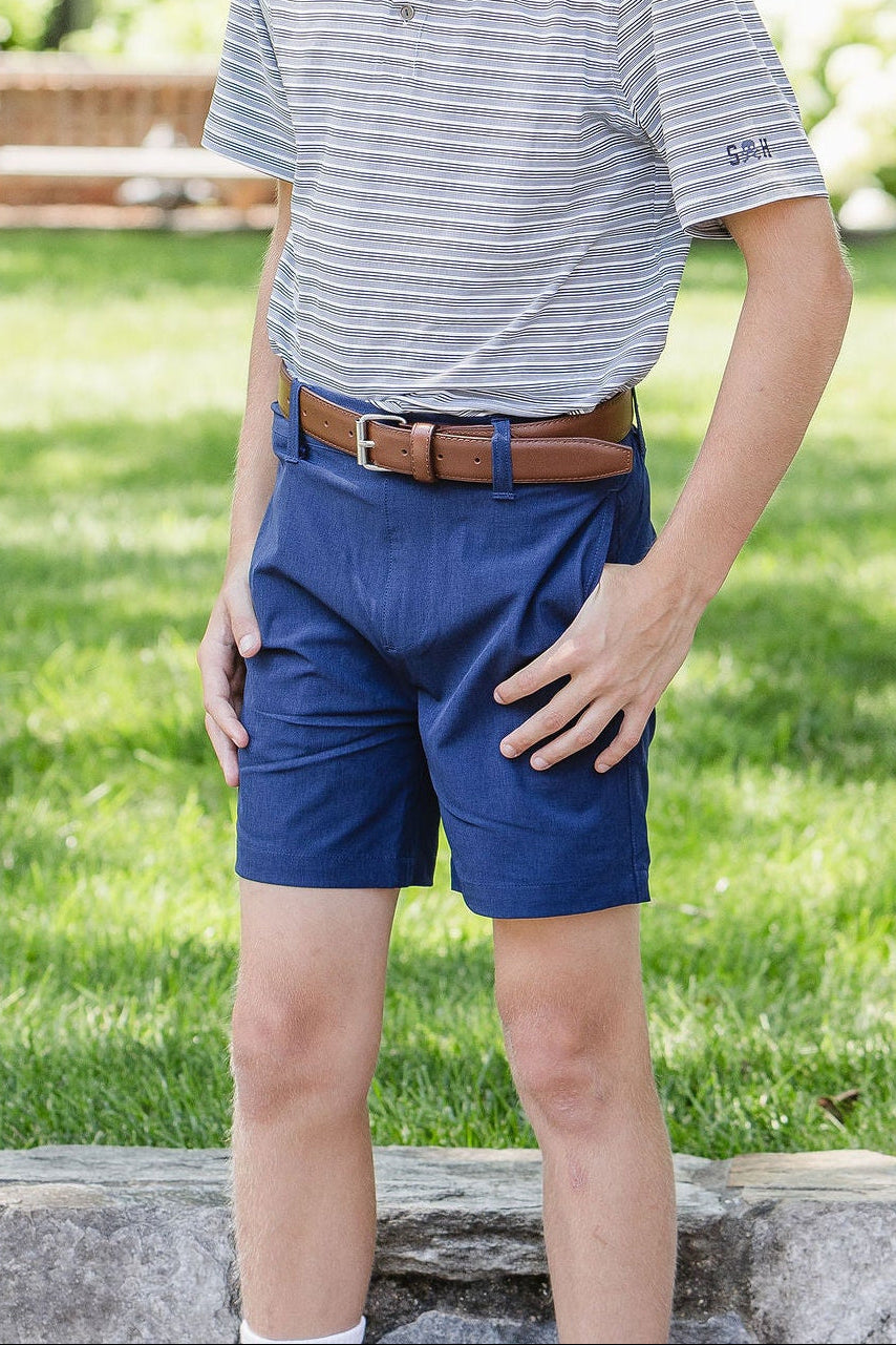 Young boy standing outdoors on a sunny day, wearing a striped polo shirt and blue shorts.
