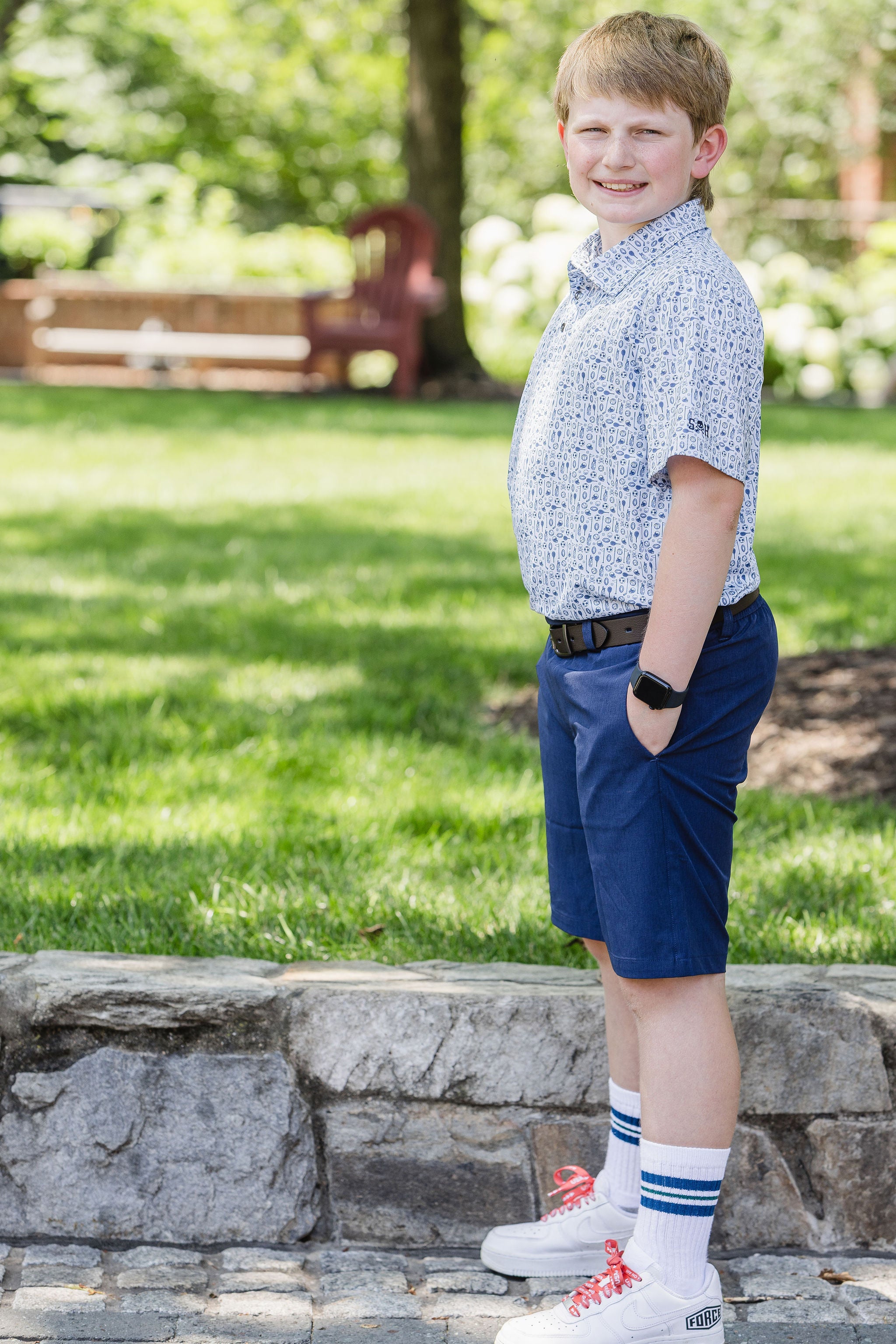 Young boy standing outdoors on a grassy area with trees in the background