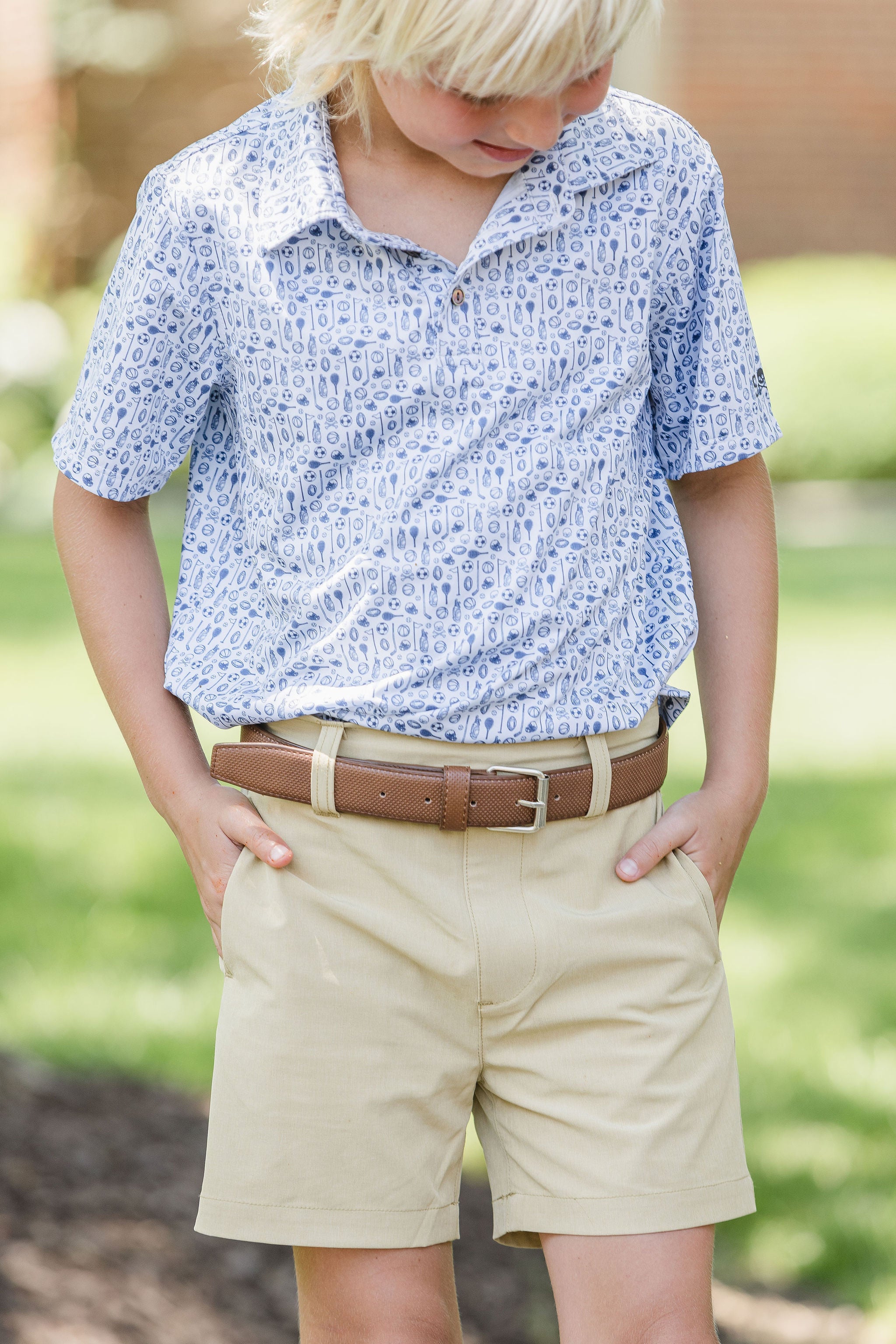 Child wearing a blue patterned shirt and beige shorts with a blurred green background