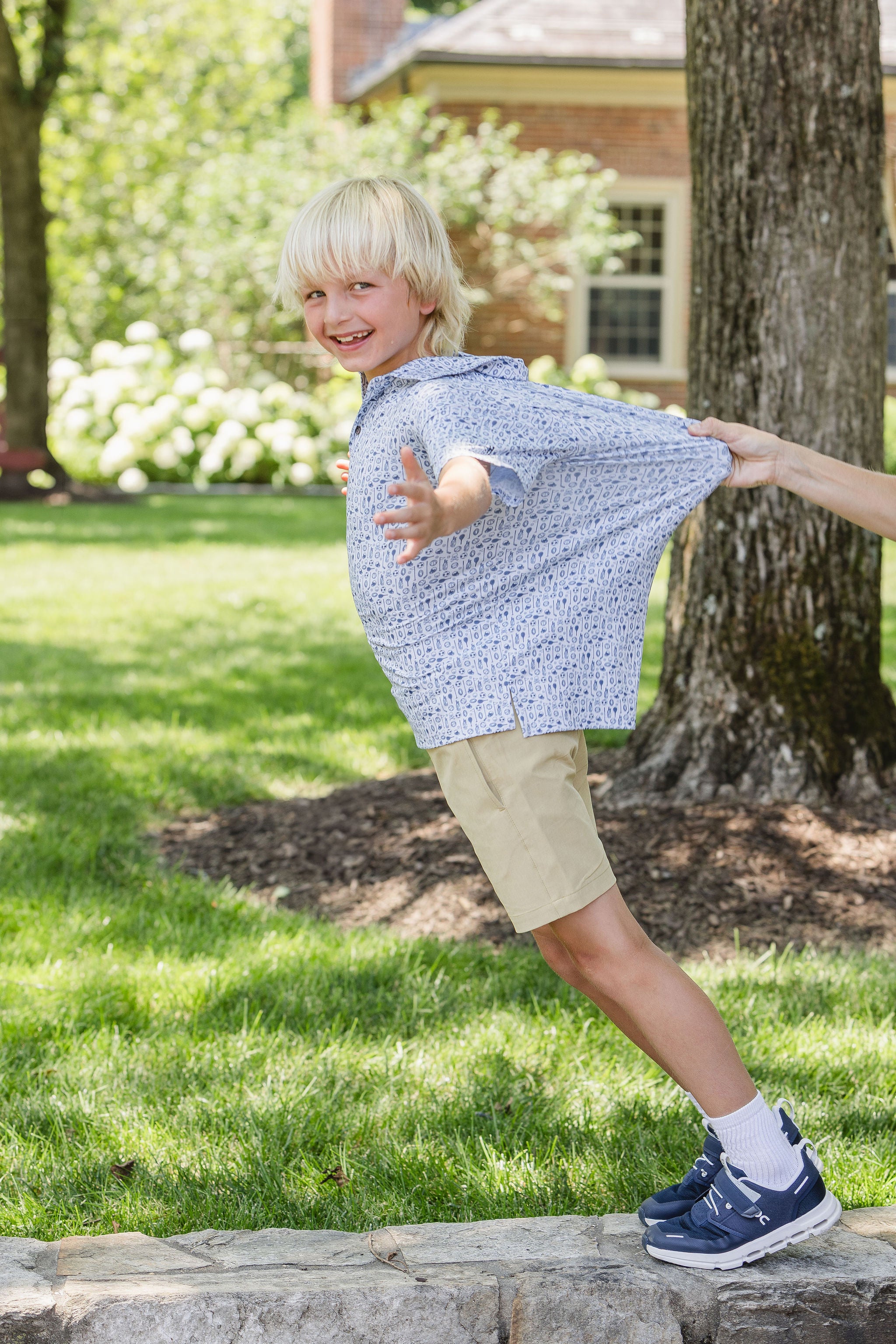Child wearing a blue patterned shirt outdoors on a sunny day being held by shirt as he's playing